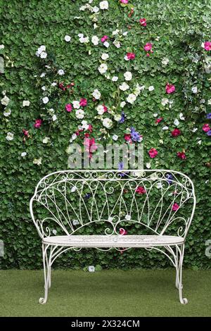 Schöne weiße Bank neben grüner Hecke mit kleinen Blumen. Stockfoto