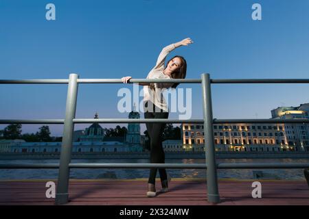 Eine junge Frau steht in Ballettstellung und benutzt als Barre das Geländer am Ufer Stockfoto