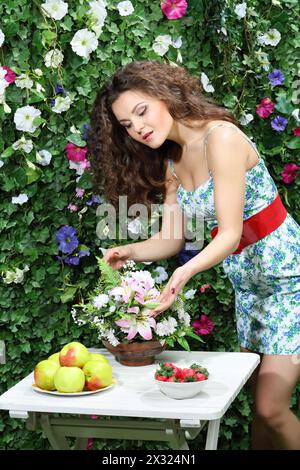 Die junge Frau berührt einen Blumenstrauß auf dem Tisch neben der grünen Hecke. Stockfoto