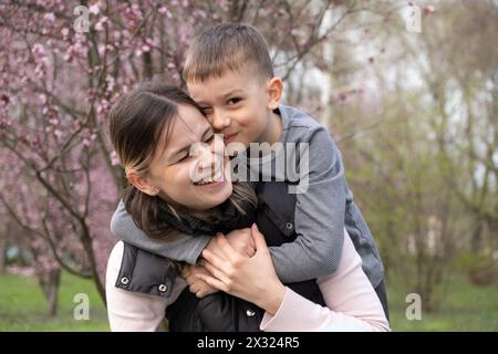 Glückliche Mutter und Sohn, die sich im Frühling zwischen Kirschblüten umarmen. Stockfoto