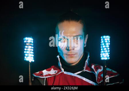 Mann mit Tattoo im Gesicht und schrecklichen Schülern in Samurai-Garderobe mit Glühstäbchen Stockfoto