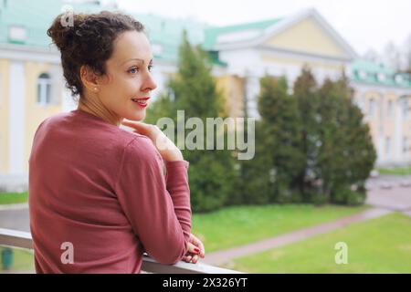 Eine junge Frau steht auf dem Balkon und beobachtet draußen auf Geländer Stockfoto