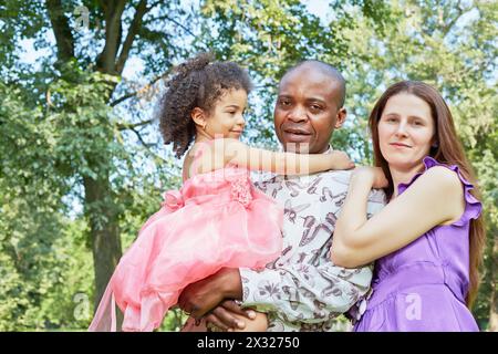 Der afrikanische Vater hält das kleine Mädchen auf den Armen, die weiße Mutter steht und kuschelt sich an ihn Stockfoto