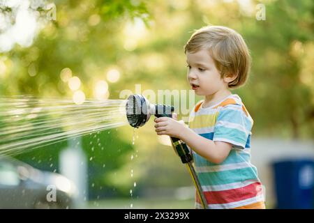 Süßer kleiner Junge, der mit Gartenschlauch an heißen Sommertagen spielt. Kinder, die im Sommer mit Wasser spielen. Aktive Freizeit mit kleinen Kindern. Stockfoto