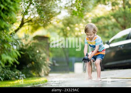 Süßer kleiner Junge, der mit Gartenschlauch an heißen Sommertagen spielt. Kinder, die im Sommer mit Wasser spielen. Aktive Freizeit mit kleinen Kindern. Stockfoto