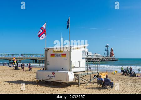 Bournemouth, Großbritannien - 30. März 2024: Ein Paar sitzt neben einem RNLI-Wachturm am West Beach vor dem Bournemouth Pier. Stockfoto