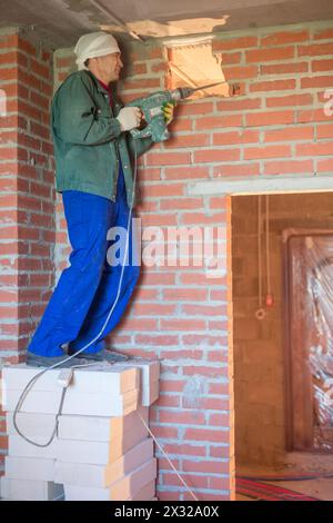 Der Arbeiter in Arbeitskleidung macht mit einem großen Perforator ein Loch in die Wand Stockfoto