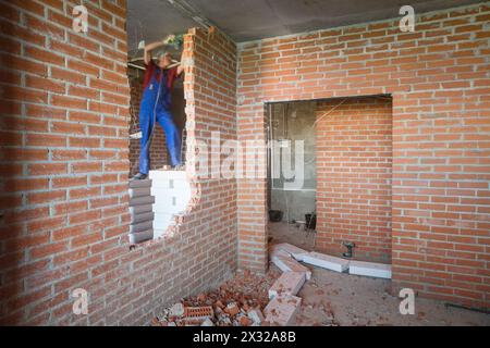 Der Arbeiter in Arbeitskleidung zerbricht die Wand mit einem großen Perforator Stockfoto