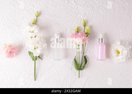 Schöner kosmetischer Hintergrund für Werbeserum, Gesichts- und Körperhautpflege Kosmetikprodukt, Spa-Produkte. Flaches Layout. Flaschen und Blumen. Stockfoto