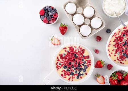 Kochen Herstellung von gebackenem Joghurt gesundes Dessert. Frau Hand kochen Ofen gebacken griechischer Joghurt Dessert mit frischen gefrorenen Beeren, auf weißem Küchentisch, mit Stockfoto