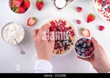 Kochen Herstellung von gebackenem Joghurt gesundes Dessert. Frau Hand kochen Ofen gebacken griechischer Joghurt Dessert mit frischen gefrorenen Beeren, auf weißem Küchentisch, mit Stockfoto