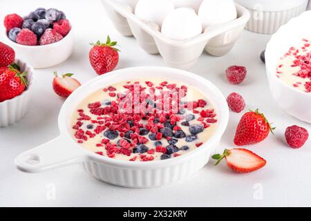Kochen Herstellung von gebackenem Joghurt gesundes Dessert. Frau Hand kochen Ofen gebacken griechischer Joghurt Dessert mit frischen gefrorenen Beeren, auf weißem Küchentisch, mit Stockfoto