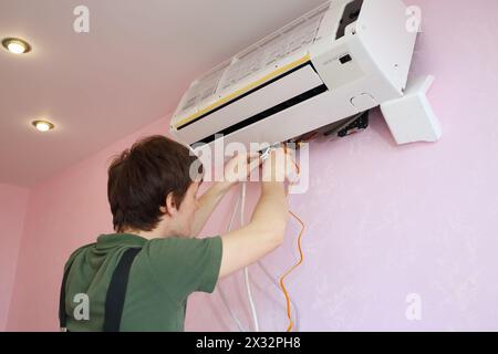 Junge Arbeiter verbinden die Kabel mit der neuen Klimaanlage im Wohnzimmer Stockfoto