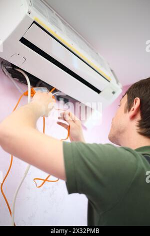 Junger Arbeiter setzt eine orange Wasserpumpe in die Klimaanlage ein Stockfoto