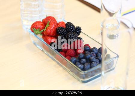 Erdbeeren, Brombeeren, Himbeeren, Heidelbeeren in einer Glasvase auf dem Schreibtisch Stockfoto