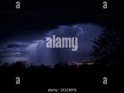 Wolken-Luft-Blitze beleuchten einen Regenschacht, der nachts aus der Sturmwolke strömt Stockfoto