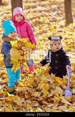 Drei kleine Kinder spielen im Herbstpark mit gelben, gefallenen Blättern, konzentrieren sich auf den Jungen auf der rechten Seite Stockfoto
