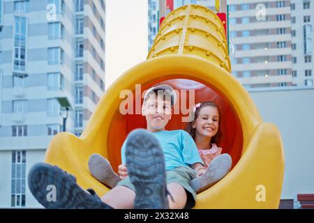 Junge und seine jüngere Schwester sitzen unten auf der Rutsche auf dem Kinderspielplatz im Hof Stockfoto