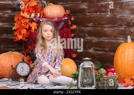 Hübsches kleines Mädchen im Kleid sitzt auf dem Boden im Zimmer mit Kürbissen und Herbsteinrichtung. Stockfoto