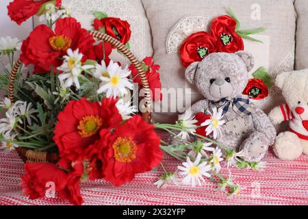 Korb mit Mohn und Gänseblümchen, dekorativen Kissen und Teddybären. Stockfoto