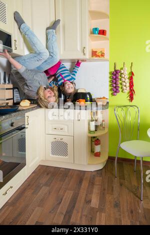 Mutter und Tochter sitzen kopfüber in den Regalen in der farbigen Küche Stockfoto