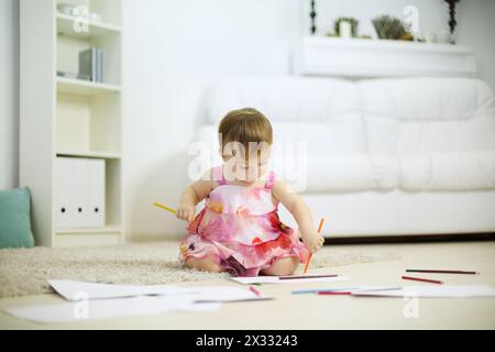 Das kleine süße Mädchen sitzt auf dem Boden und zeichnet mit Bleistift im Zimmer zu Hause. Geringe Schärfentiefe. Stockfoto