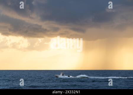 Ein Fischerboot fährt bei Sonnenaufgang am South Ponte Vedra Beach entlang der Küste, während eine sich nähernde Wolke eine Regensäule über dem Meer abwirft. (USA) Stockfoto