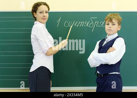 Junge und Lehrer stehen in der Nähe der grünen Tafel mit der Aufschrift September 1 im Klassenzimmer der Schule. Fokus auf Frau. Stockfoto