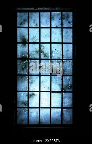 Großes altes, schmutziges Fenster mit blauen, zerkratzten Gläsern im dunklen Zimmer. Stockfoto
