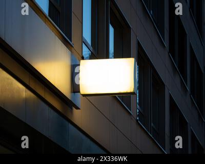 Beleuchtetes Firmenschild bei Nacht an einer Gebäudewand. Leeres Werbemockup-Schild an der Außenseite eines Bürokomplexes als Kopierraum. Stockfoto