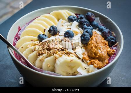 Smoothie-Schüssel mit Acai-Pulver, Heidelbeeren, Erdnussbutter, Banane, gerösteten Kokosflocken und Granola. Stockfoto