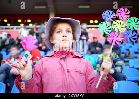 Mädchen in rosa Jacke und panamahut mit Ratsche und Windspinner in den Händen im Stadion Stockfoto