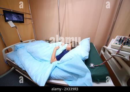 Junge, der auf dem Bett liegt und auf einer Krankenhausstation fernsieht Stockfoto