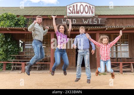 Vierköpfige Familie, die auf dem Hintergrund des Wildwest-Saloons springt Stockfoto