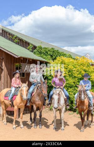 Vierköpfige Cowboyfamilie auf Pferden auf dem Hintergrund eines Holzgebäudes Stockfoto