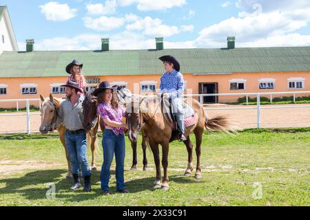 Vierköpfige Cowboyfamilie mit Pferden auf Gras Stockfoto