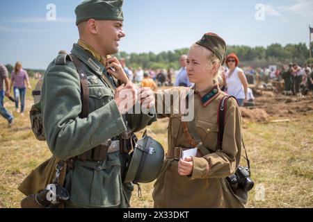 NELIDOVO, RUSSLAND, 12. JULI 2014: Sowjetisches Soldatenmädchen richtet Uniform eines deutschen Soldaten auf dem Schlachtfeld 2014 auf Stockfoto