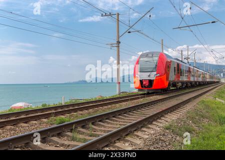 Der rote Zug fährt auf Schienen entlang der Küste Stockfoto