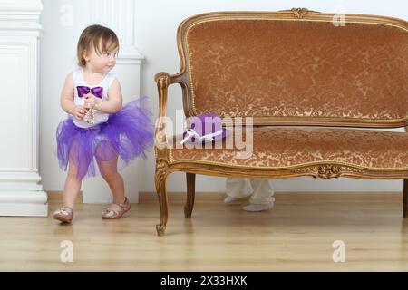 Kleines Mädchen in lila Rock, das vor dem Jungen um das Sofa läuft Stockfoto