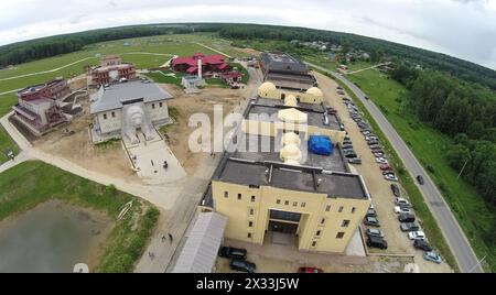 RUSSLAND, BOROVSK - 13. JUN, 2014: Die Menschen gehen am Kulturkomplex Ätnomir vorbei, mit vielen Autos auf großen Parkplätzen am Sommertag. Luftaufnahme. Foto mit Rauschen f Stockfoto