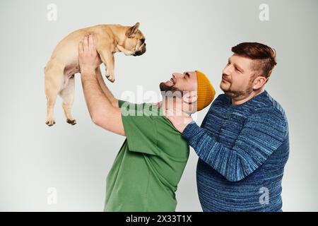 Zwei Männer halten eine französische Bulldogge in einem zärtlichen Moment zart nah an sein Gesicht. Stockfoto