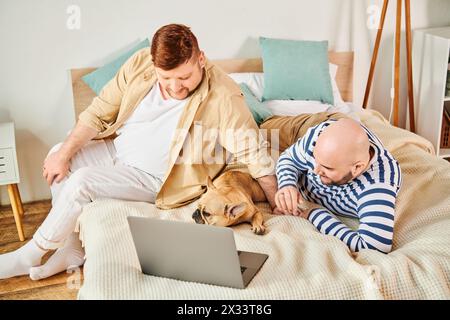 Zwei Männer und ein Hund entspannen sich auf einem Bett mit Laptop. Stockfoto