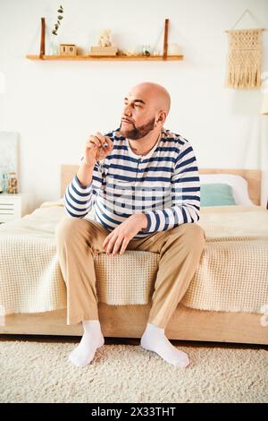 Ein stilvoller Mann in Brille sitzt auf einem Bett in einem modernen Schlafzimmer und besinnt den Tag. Stockfoto