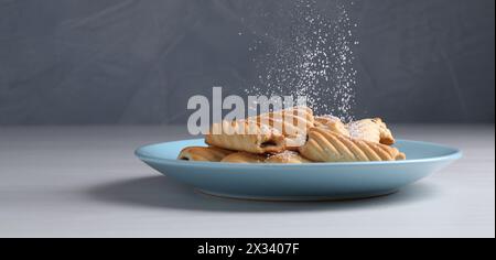Frau mit einem Sieb, das Puderzucker auf Kekse streut, an weißem Holztisch, Nahaufnahme Stockfoto