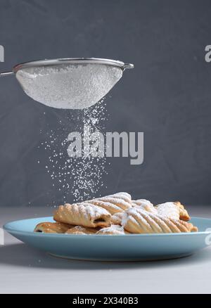 Frau mit einem Sieb, das Puderzucker auf Kekse streut, an weißem Holztisch, Nahaufnahme Stockfoto