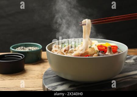 Heiße Ramen mit Stäbchen am Holztisch essen, Nahaufnahme. Nudelsuppe Stockfoto