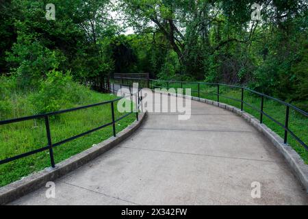 Ein gewundener Betonweg wird von Metallgeländern flankiert und von üppigem Grün umgeben. Das geschwungene Design führt den Blick durch die Landschaft. Stockfoto