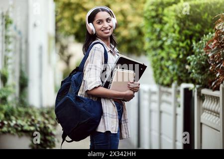 Student, Mädchen und Rucksack auf dem Campus mit Lächeln, Kopfhörern und Büchern zum Lernen, zur Entwicklung und zum Lernen. Weibliche Person, glücklich und Universität für Stockfoto