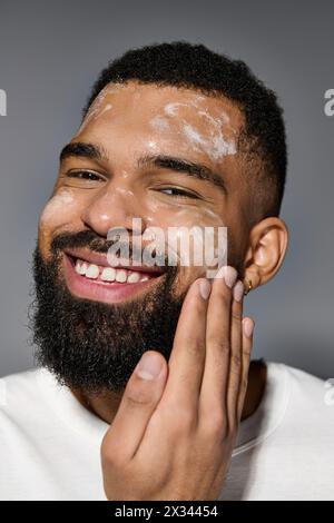 Ein ansprechender Mann mit Bart in weißem T-Shirt, der sich auf die Hautpflegeroutine konzentriert. Stockfoto