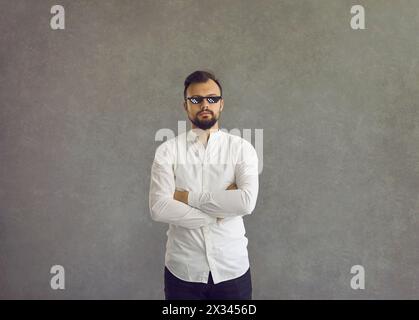 Junger Mann in einer Lebensbrille, die Arme überkreuzt auf grauem Hintergrund Stockfoto